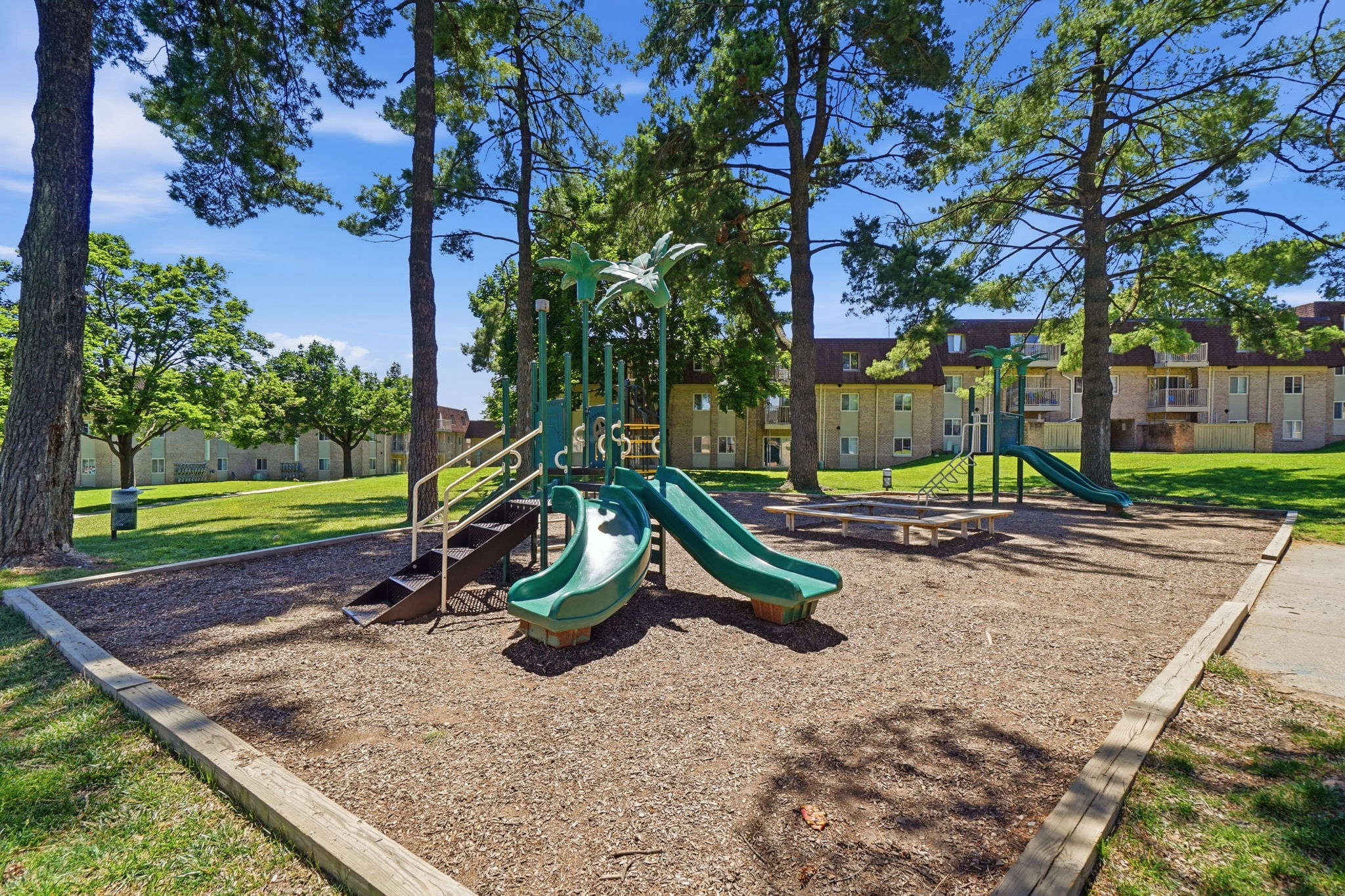 A playground with a green slide and a wooden fence.